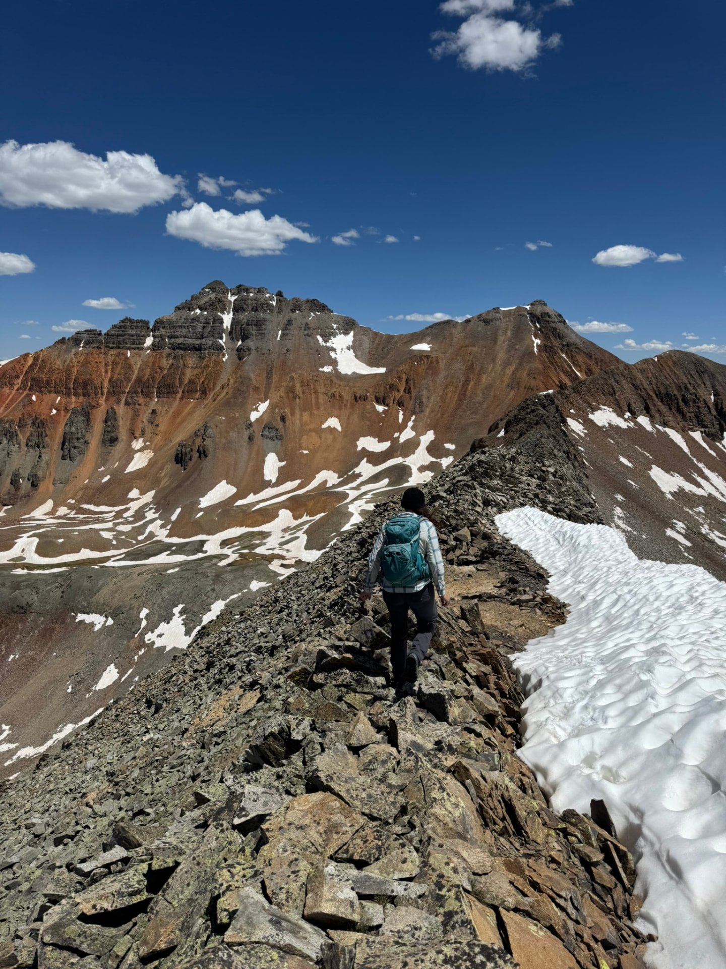 Hiker on a rocky ridgeline beneath snow-streaked San Juan peaks
