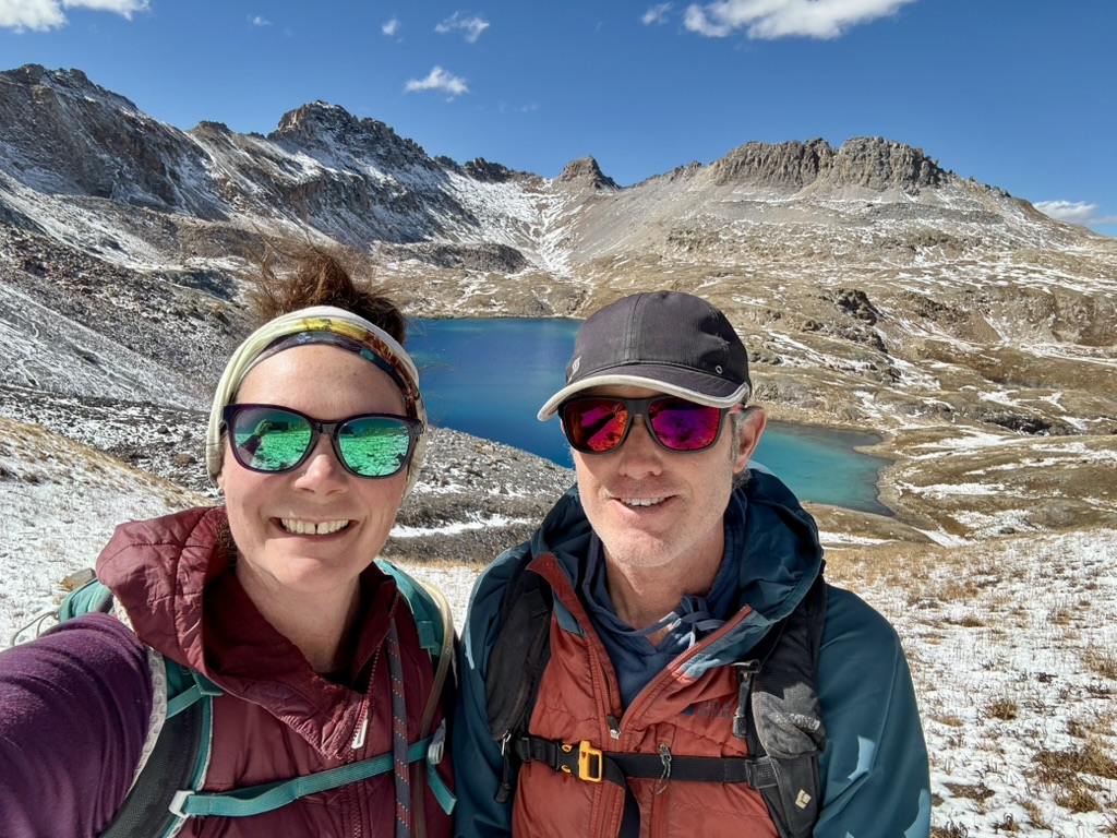 Michelle and her partner hiking near a turquoise alpine lake in the Colorado mountains